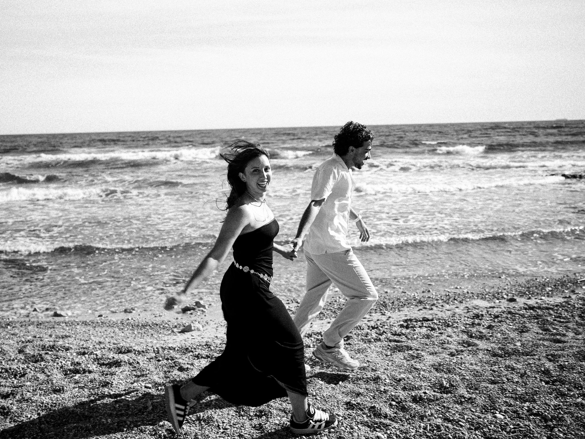 Les mariés courent sur la plage en riant, en noir et blanc